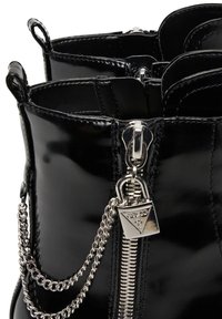 Stivali alla caviglia in pelle verniciata nera con zip argentata, accentuati da una catena e un lucchetto decorativo. Texture liscia con una finitura lucida.