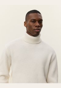 White ribbed turtleneck sweater made from a soft material. Features a high collar and relaxed fit with prominent texture throughout.
