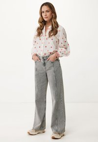 Blusa bianca con motivi a rombi rossi, maniche a palloncino e chiusura con bottoni, abbinata a pantaloni a vita alta grigi chiari a gamba larga e sneakers.