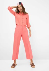 Coral linen shirt and wide-leg pants set with a button closure, featuring rolled sleeves and a smooth texture, complemented by brown slide sandals.