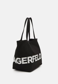 Czarna torba na ramię z długimi rączkami, z odważnym białym napisem "LAGERFELD" z jednej strony. Obszerny kształt i miękka faktura.