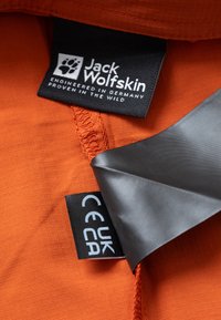 Oranje stof met een gestructureerd oppervlak, voorzien van een "Jack Wolfskin" label en verzorgingsetiketten in zwart en wit, met een gestikt randje.
