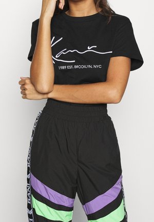 Black cotton t-shirt with white cursive logo and text. Black pants with colorful chevron patterns in green, purple, and black. Stretch waistband.