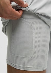 Šviesiai pilki sportiniai šortai su tekstūruotu akiniu kišeniu šone. Audinys lygus, su prigludusiu dizainu ir tvarkingais siuvimo detalėmis.