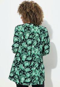 Blusa nera con motivo floreale verde, con maniche lunghe, una vestibilità comoda e dettagli plissettati sul retro, realizzata in tessuto leggero.