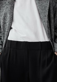 Zwarte broek met plooien, gedragen met een eenvoudige witte blouse, bovenop een zwart-wit hertenpunt blazer. Gestructureerde stof en op maat gemaakte pasvorm.