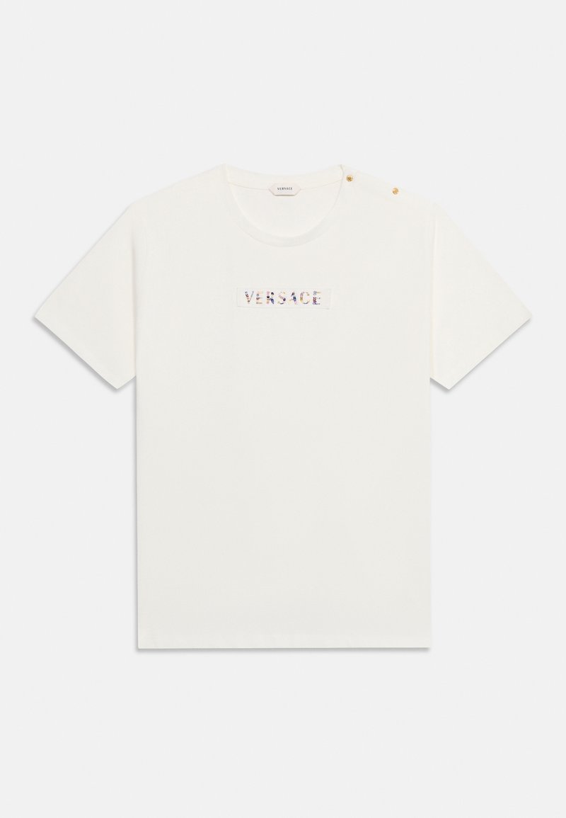 Λευκό T-shirt με κοντό μανίκι και στρογγυλή λαιμόκοψη, κείμενο "VERSACE" με πολύχρωμο σχέδιο στο στήθος και δύο μικρά χρυσά κουμπιά στον αριστερό ώμο.