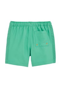 Žiarivo zelené šortky s elastickým pásom, s bočnými panelmi z oka a zadným vreckom, v ktorom sa nachádzajú dve malé oranžové očká blízko dna.