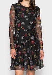 Robe noire avec de longues manches transparentes, ornée d'un motif floral en rouge, jaune et blanc. Corsage ajusté et jupe évasée.
