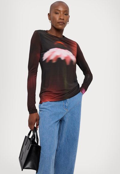 Maglietta a maniche lunghe con un motivo floreale sfocato in tonalità di rosa e rosso su sfondo nero, abbinata a jeans in denim blu a vita media e a una borsa nera.