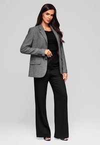 Šedý strukturovaný blazer s klopami, v kombinaci s černými širokými kalhotami. Blazer má dvě přední kapsy a přiléhavý střih.