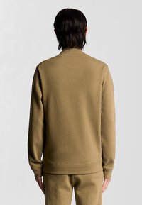 Felpa beige con colletto alto, realizzata in materiale testurizzato. Il design presenta maniche lunghe e una vita aderente.