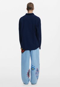 Marineblå ribbet strikket skjorte med krave, parret med lyseblå vide jeans med farverige broderede mønstre.