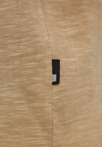 Tissu beige texturé avec une couture latérale et une petite étiquette rectangulaire noire et blanche attachée près de la couture.