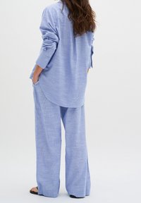 Světle modrá volná košile a odpovídající široké kalhoty, vyrobené z texturované látky s jemným pruhovaným vzorem. Košile má ohrnuté rukávy a kapsy.