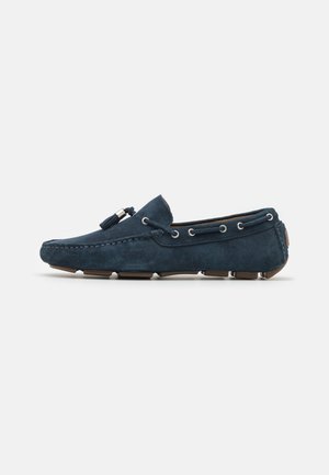 Navy blauwe suède mocassinschoenen met zilveren hardware, ronde neus, decoratieve stiksel en rubberen zool met profiel voor grip.