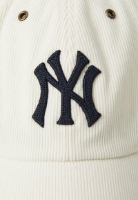 Fehér kordbársony baseball sapka sötét navy hímzett "NY" logóval az elején. Kiegészítők között szerepel sárgaréz szellőzőlyukak.