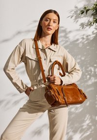 Brown leather handbag with dual handles and adjustable shoulder strap. Features front zipper pocket and side compartment. Textured finish.