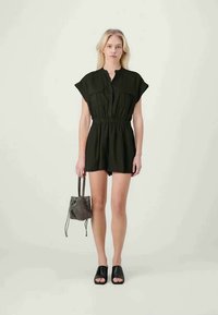 Black, knee-length romper with cap sleeves, front pockets, elastic waist, and a relaxed fit. Paired with a textured crossbody bag and sandals.