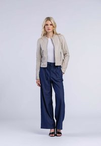 Ljusbeige läderjacka, vit åtsittande skjorta, lösa marinblå vida byxor, svarta remsandaler; enkel design utan synliga dekorationer.
