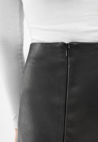 Musta nahkahame, jossa on selkävetoketju, sileä pinta ja puhtaat linjat, osittain näkyvissä valkoista taustaa vasten.