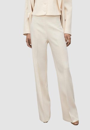 Pantalones beige de corte ajustado con cintura alta, piernas rectas y una textura sutil. Complementados con una blazer de color claro a juego.