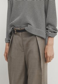 Maglia a righe bianco e nera in maglia abbinata a pantaloni beige chiaro sartoriali. Include una cintura nera con una fibbia dorata. Tessuto testurizzato, vestibilità rilassata.