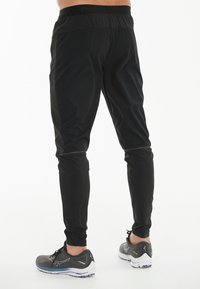 Svarta idrottsbyxor med en åtsittande design, med ett brett elastiskt midjeband och kontrasterande sömmar. Matchas med grå löparskor.