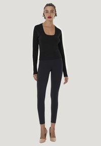 Sort ribbet bluse med lange ærmer og firkantet udskæring, kombineret med mørke leggings og nøgne højhælede sko. Simpelt og tætsiddende design.