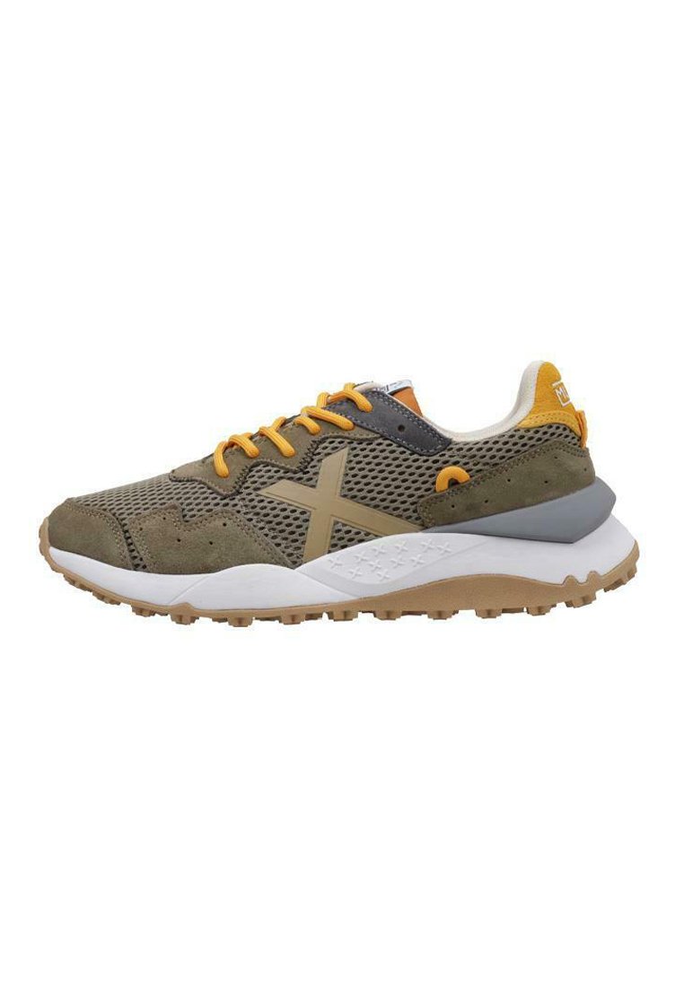 Zapatillas deportivas con una parte superior de malla transpirable en verde y gris con acentos amarillos, una suela blanca acolchada y una suela exterior texturizada en color marrón claro.