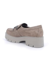Scarpa slip-on in suede marrone chiaro, con una spessa suola grigia e una fibbia metallica decorativa sulla fascia superiore.