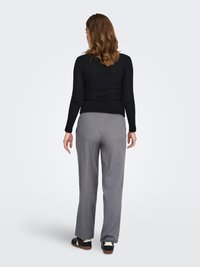 Haut noir à manches longues côtelé, pantalon gris plissé à coupe droite, et chaussures noires avec des accents blancs vus de dos.