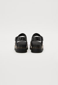 Svarta sandaler med en tjock sula, spänne och öppen bakdesign. Slät läderövre med kontrasterande sömmar längs sulan.
