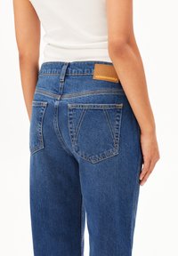 Jeans en denim bleu avec une taille haute, jambe droite et deux poches arrière. Dotés d'une étiquette en cuir beige portant la mention "ARMEDANGELS."
