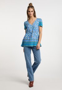 Světle modrý květinový peplum top s krátkými rukávy, výstřihem do V, stahovací pas a vzorovaným lemem; spárovaný s modrými džíny rovného střihu a hnědými botami.
