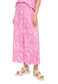 Lichte, roze stoffen rok met een wit bloemenpatroon en een elastische tailleband, gecombineerd met beige gevlochten sandalen met een dikke zool.