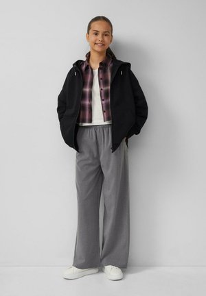 Schwarze Kapuzenjacke, lila karierte Hemd mit Knopf, weißes T-Shirt, graue weit geschnittene Hose und weiße Turnschuhe. Einfaches, lässiges Outfit.