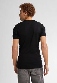Tricou negru cu mânecă scurtă, guler rotund, fabricat din material neted, purtat cu blugi gri, arătând o vedere din spate simplă.