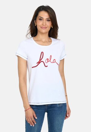 Camiseta de algodón blanca con cuello redondo y mangas cortas, con bordados en rojo y negro formando la palabra "hola" en el frontal.