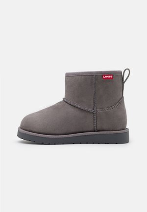 Bottine en daim gris avec semelle plate noire, boucle à tirer au talon et étiquette rouge avec le logo Levi's sur le col.