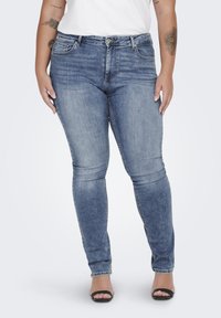 Jeans ajustados de mezclilla azul con una cintura de altura media, bolsillos frontales y un sutil detalle desgastado. Se estrechan en el tobillo con una textura suave.