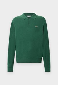 Zaļš adīts polo džemperis ar apkakli, trīs pogu aizdari un Lacoste logotipu. Iekļauj ribotas piedurknes un apakšu, nodrošinot pieguļošu izskatu.