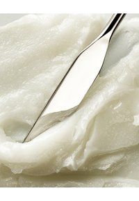 Un couteau métallique avec une lame lisse et brillante coupe à travers une substance épaisse, blanche et crémeuse, avec une texture brillante et une consistance douce.