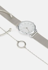 Silver mesh strap watch with a white face and minimalistic design, paired with a silver bracelet featuring a circular charm with rhinestones.