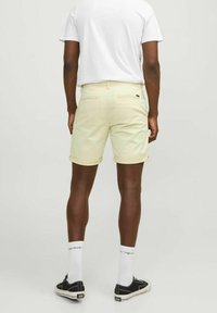 Světle žluté šortky vyrobené z bavlny, s ohrnutým lemem, dvěma zadními kapsami a malou značkovou nášivkou na pase. Vytvořené s bílým tričkem.