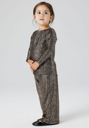 Ensemble en deux pièces en tissu brun scintillant comprenant des manches longues et un pantalon ample, associé à des chaussures noires. Texture lisse dans l'ensemble.