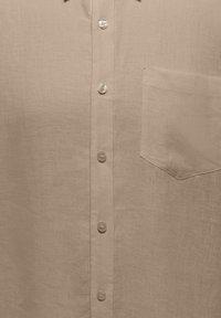 Chemise en lin beige vue de face avec cinq boutons visibles et une poche poitrine unique du côté droit.