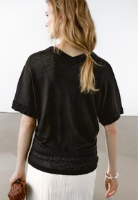 Svart löst sittande t-shirt med korta uppvikta ärmar, v-ringad design, mjukt material, bärs över en vit texturerad kjol.