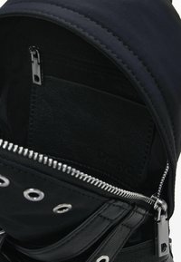 Mustmust mustrohke välispinna, hõbedased tõmblukud ja nahkdetailid. Omab korralduseks sisemist tõmblukuga taskut.