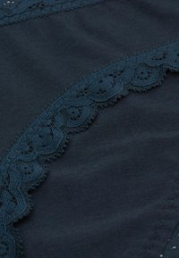 Marine stof met delicate kantafwerking met geschulpte randen en bloemmotieven. Gladde textuur met een ondoorzichtige afwerking en ingewikkelde details.